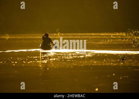 Malerische Aussicht auf Fischer im Kanu bei orangefarbenem Sonnenaufgang auf dem Fluss Stockfoto