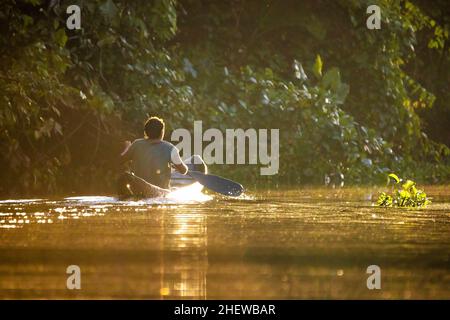 Malerische Aussicht auf Fischer im Kanu bei orangefarbenem Sonnenaufgang auf dem Fluss Stockfoto