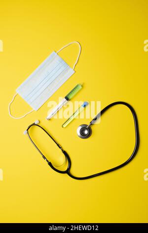 Medizinische Geräte auf gelbem Hintergrund, Maske, Spritze und Stethoskop, Draufsicht Stockfoto