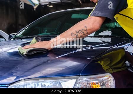 Mann, der in der Autowerkstatt arbeitet. Reiben und polieren blaue Motorhaube oder Motorhaube mit ihm Hand zu bekommen sauber, Glanz und Glanz. Geeignet für Lackarbeiten und Stockfoto