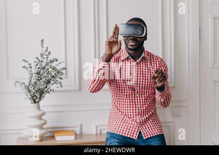 Aufgeregt fröhlicher afrikanischer Mann trägt VR-Brille total in Augmented Reality von 3D Spielen eingetaucht Stockfoto