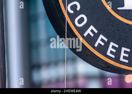 Hängende Neonwerbung aus dem Café im Hintergrund der Stadt mit sanftem Fokus Stockfoto
