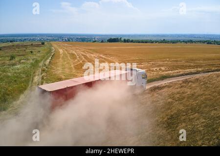 Luftaufnahme eines LKW-Lastwagens auf unbefestigten Straßen zwischen landwirtschaftlichen Weizenfeldern. Transport von Getreide nach der Ernte durch Mähdrescher harv Stockfoto