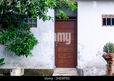 Braune Holztür steht auf weißer rauer Wand an der Seite des Hauses Stockfoto