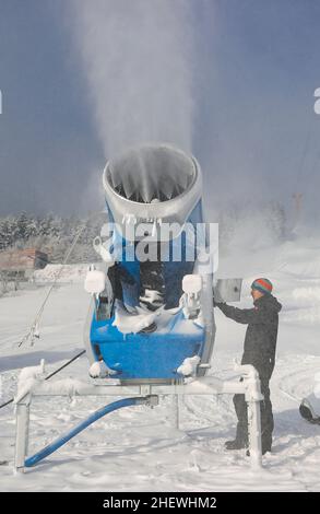 12. Januar 2022, Sachsen, Oberwiesenthal: Ein Mitarbeiter der Liftgesellschaft Oberwiesenthal stellt am Hang des Fichtelbergs eine Schneekanone ein. Am Samstag (15,01.) startet die diesjährige Skisaison am Fichtelberg offiziell. Aufgrund von Corona ist das Skigebiet nur für geimpfte und geborgene Skifahrer geöffnet (2G); beim Anstehen am Lift und im Lift selbst muss eine Maske getragen werden. Der Status von 2G wird vor dem Kauf des Skipasses sowie im Skigebiet überprüft. Zu diesem Zweck werden auf dem Parkplatz des Fichtelbergs ca. eine Kontrollstelle und eine zentrale Verkaufsstelle für Lifttickets eingerichtet Stockfoto