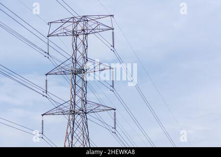 Ein massiver und hoher Metallrahmen für den elektrischen Turm verteilt die Spannungsenergie mit den gestreckten Kabeln darüber, steht unter dem klaren und Stockfoto