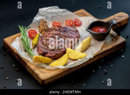 Rindersteak mit Zweig Rosmarin und Kartoffeln auf einem Holztisch. Stockfoto