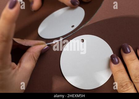 Weiße Pappe Marke blank Tag der runden Form auf braunem Hintergrund mit weiblichen Händen halten Spiegel in der Nähe Tag zeigt seine Reflexion positioniert. Tag Stockfoto