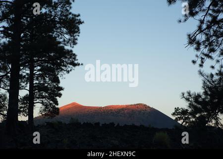 Blick auf den Zimtkegelvulkan des Sunset Crater, während die untergehende Sonne den Kraterrand rot glühen lässt. Stockfoto