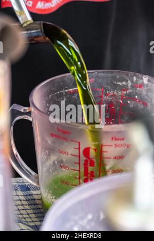 Nahaufnahme eines Gießen eines grünen Tees oder Matcha-Wassers in eine transparente Kunststoff-Messbecher für einen thai-Tee mit verschwommenem und weichem Fokus Hintergrund Stockfoto