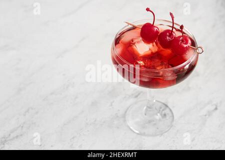 Ein Glas vereisten Manhattan-Cocktails mit Kirschen auf hellem Hintergrund, Nahaufnahme Stockfoto