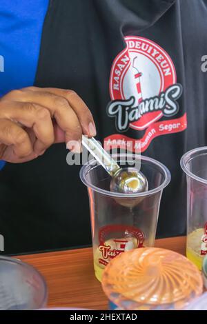 Gießen eines Basilikums mit Edelstahllöffel in ein transparentes Kunststoffglas Stockfoto