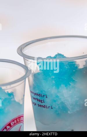 Kaltrasierte Eiswürfel mit gegossenem blauem Sirup für einen frischen blauen Mojito-Drink in transparentem Kunststoffglas Stockfoto