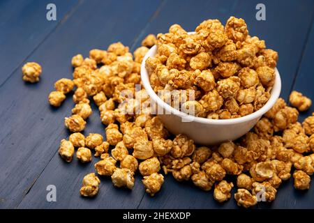 Karamell Popcorn in weißer Schale auf rustikalem blauen Holztisch. Nahaufnahme. Kopieren Sie Platz für Ihren Text Stockfoto