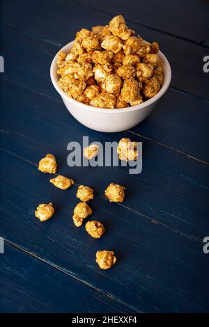 Karamell Popcorn in weißer Schale auf rustikalem blauen Holztisch. Nahaufnahme. Kopieren Sie Platz für Ihren Text Stockfoto