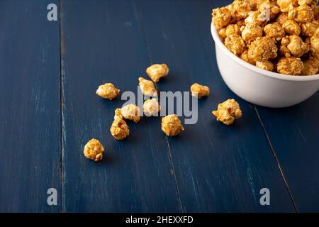 Karamell Popcorn in weißer Schale auf rustikalem blauen Holztisch. Nahaufnahme. Kopieren Sie Platz für Ihren Text Stockfoto