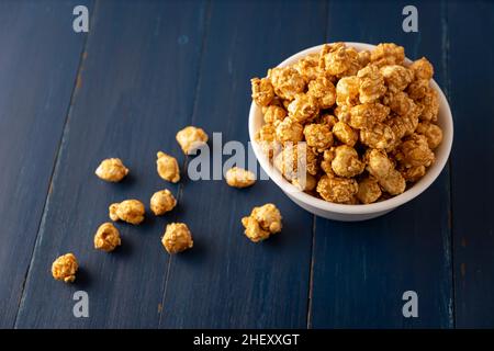 Karamell Popcorn in weißer Schale auf rustikalem blauen Holztisch. Nahaufnahme. Kopieren Sie Platz für Ihren Text Stockfoto