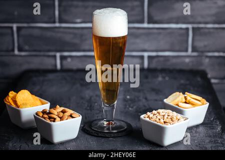 Ein Glas Bier mit Schaum und vier verschiedene Snacks Stockfoto