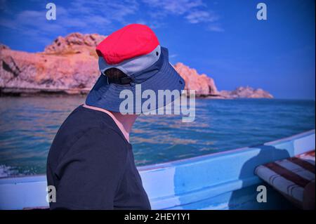 Rückansicht einer Frau, die auf dem Boot sitzt und die Küste entlang segelt Stockfoto