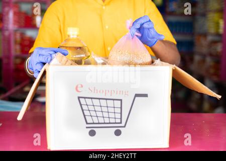 Nicht erkennbarer Lebensmittelgeschäft oder Kirana Händler mit Schutzmaske Verpackung Lebensmittel auf E-Shopping-Box - Konzept des E-Commerce, Online-Shopping Stockfoto