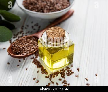 Leinsamen oder Leinsamen in Löffel und Schüssel mit Glas Leinöl auf Holzkulisse Stockfoto