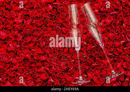 Zwei leere Sektgläser auf rotem Rosenhintergrund zum Jubiläum und Valentinstag-Konzept. Stockfoto