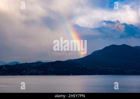 Über den Bergen rund um den Lago Maggiore taucht ein farbenfroher Regenbogen auf. Stockfoto
