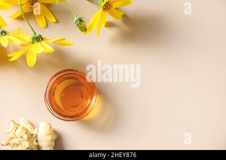 Jerusalemer Artischockensirup in Schale, Blumen und Wurzel auf beigem Hintergrund. Speicherplatz kopieren. Blick von oben. Stockfoto