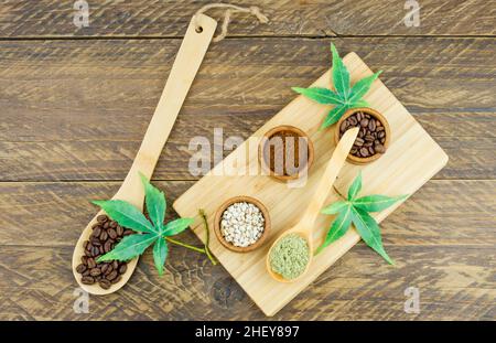 Draufsicht auf das Kaffeesortiment in Mini-Schüsseln und Holzlöffeln mit Connabis-Samen und Blättern. Brauner Hintergrund aus Holz Stockfoto