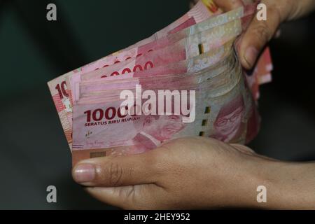 Frau zeigt Rupiah indonesisches Geld isoliert auf dunklem Hintergrund Stockfoto