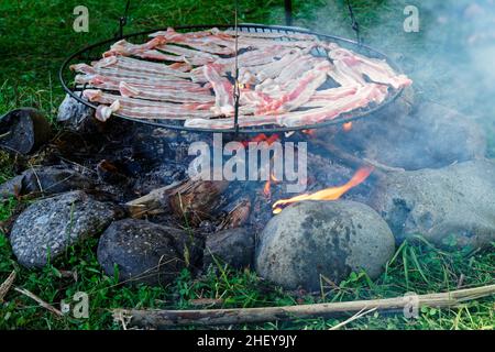 Der Speck brutzelt am offenen Feuer, Camping auf dem Land, Neuseeland. Stockfoto