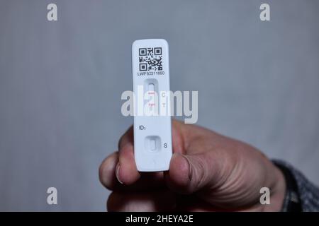 Weiblicher Hand-Selbsttest mit Coronavirus-Lateral-Flow-Antigen mit positivem Ergebnis und grauem, schlichtem Hintergrund Stockfoto