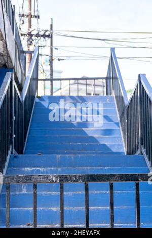 Blaue Treppe mit schwarzem Eisengriff und hellem Sonnenlicht am Morgen Stockfoto