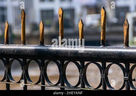 Nahaufnahme eines schwarzen eisernen Zauns mit golden scharfen Stangen auf dem Stadtfluss mit verschwommenem und weichem Fokushintergrund Stockfoto