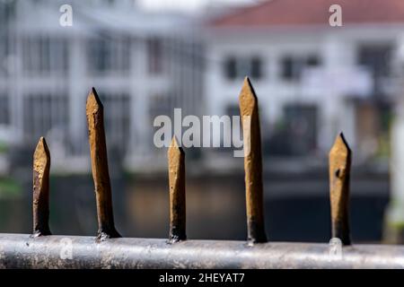 Nahaufnahme eines schwarzen eisernen Zauns mit golden scharfen Stangen auf dem Stadtfluss mit verschwommenem und weichem Fokushintergrund Stockfoto