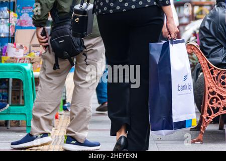 Moderne Arbeiterinnen, die eine Einkaufstasche in der Hand halten und auf den überfüllten Gehwegen spazieren Stockfoto