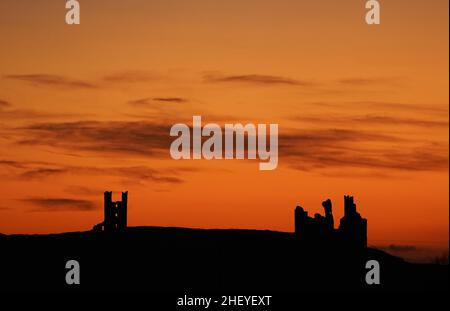 Die Sonne geht über den Ruinen der Burg von Dunstanburgh an der Küste von Northumberland auf, nachdem ein weiterer kalter Start in den Tag im ganzen Land möglich war. Bilddatum: Donnerstag, 13. Januar 2022. Das Schloss aus dem 14th. Jahrhundert gehört dem National Trust und wird von English Heritage verwaltet. Stockfoto