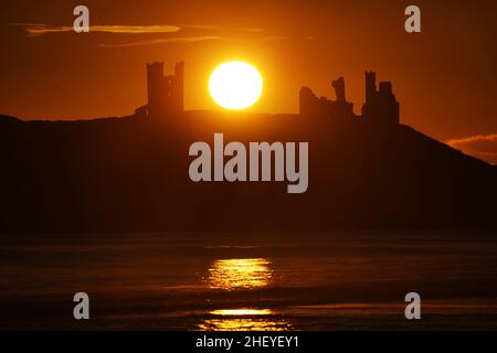 Die Sonne geht über den Ruinen der Burg von Dunstanburgh an der Küste von Northumberland auf, nachdem ein weiterer kalter Start in den Tag im ganzen Land möglich war. Bilddatum: Donnerstag, 13. Januar 2022. Das Schloss aus dem 14th. Jahrhundert gehört dem National Trust und wird von English Heritage verwaltet. Stockfoto