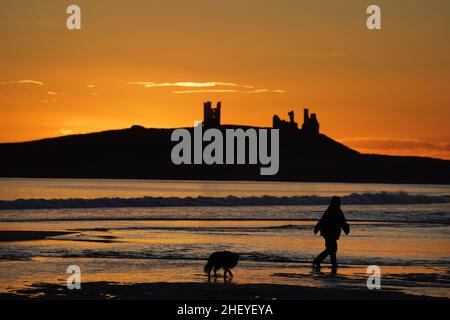 Die Sonne geht über den Ruinen der Burg von Dunstanburgh an der Küste von Northumberland auf, nachdem ein weiterer kalter Start in den Tag im ganzen Land möglich war. Bilddatum: Donnerstag, 13. Januar 2022. Das Schloss aus dem 14th. Jahrhundert gehört dem National Trust und wird von English Heritage verwaltet. Stockfoto