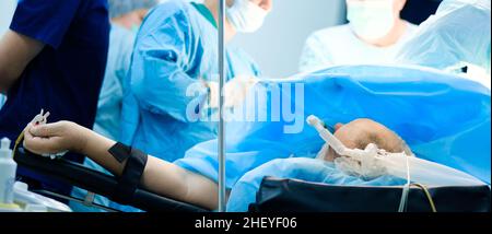 Während der Operation liegt eine unbekannte Person auf dem Operationstisch. Selektiver Fokus. Der Patient ist bewusstlos und an das künstliche Beatmungssystem der Lunge angeschlossen. Unscharfer Hintergrund. Breitbild. Stockfoto