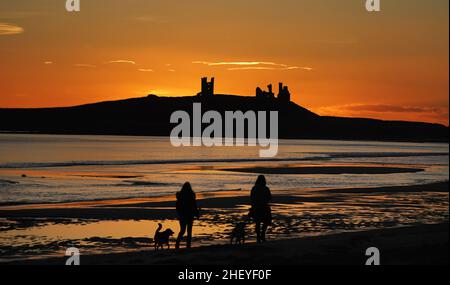 Die Sonne geht über den Ruinen der Burg von Dunstanburgh an der Küste von Northumberland auf, nachdem ein weiterer kalter Start in den Tag im ganzen Land möglich war. Bilddatum: Donnerstag, 13. Januar 2022. Das Schloss aus dem 14th. Jahrhundert gehört dem National Trust und wird von English Heritage verwaltet. Stockfoto