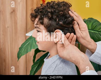 Hörlösungen für Kinder. Der Audiologe passt ein Hörgerät auf das männliche Kinderohr, während er eine Hörklinik besucht Stockfoto