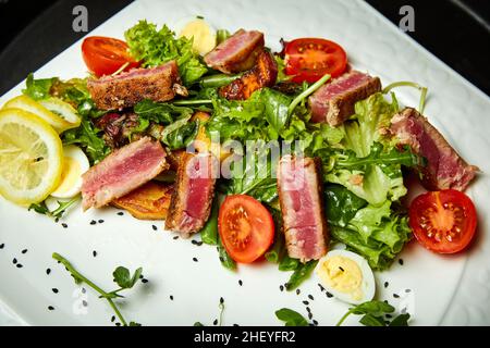 Salat mit Thunfisch, Salat, Kirschtomaten, Kartoffeln und Wachtelei verrühren. Nahaufnahme, selektiver Fokus Stockfoto