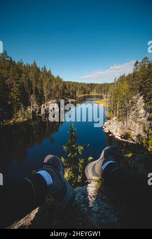 Traveller sitzt auf einem hohen Felsen und beobachtet einen wunderschönen natürlichen See im hiidenportti Nationalpark, Sotkamo in der region kainuu, Finnland. Wandern auf der Finni Stockfoto