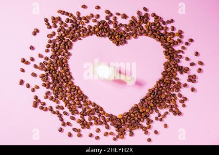 Tasse Kaffee auf einem violetten Hintergrund mit einer Form aus Kaffeebohnen. Ideales Konzept für Cheer Coffee Day, internationalen Barista Day o Stockfoto