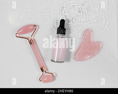 Pipette mit Feuchtigkeitscreme und Massagezubehör aus Gua Sha in Wasser. Das Konzept des Minimalismus. Stockfoto