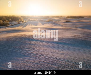 Winter-Luftpanorama mit welligen, schneebedeckten Wiesen, frühmorgendliches Licht, frühem Frühling Stockfoto