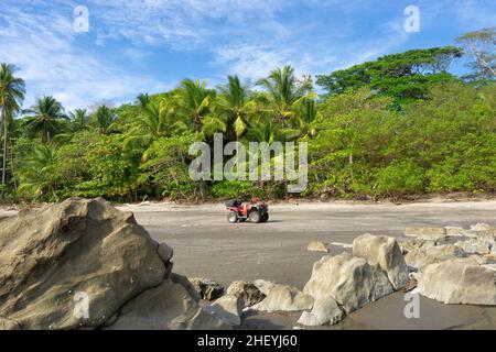 Rotes Quad-Bike auf einem felsigen Strand von Costa Rica vor grünem Hintergrund Stockfoto