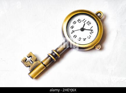 Nahaufnahme eines bronzefarbenen Schlüsselanhänger in Form einer Uhr im Vintage-Stil, der auf einem Betonhintergrund liegt. Zeitmanagement-bezogenes Konzept. Stockfoto