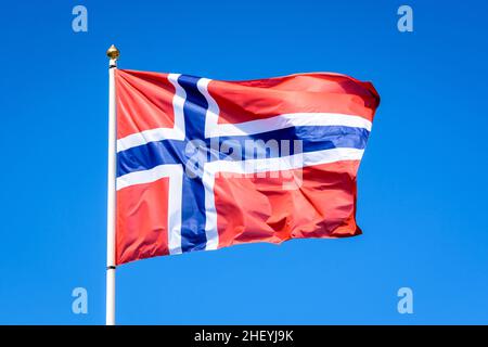 Die Nationalflagge Norwegens fliegt im Wind mit vollem Mast gegen den blauen Himmel. Stockfoto